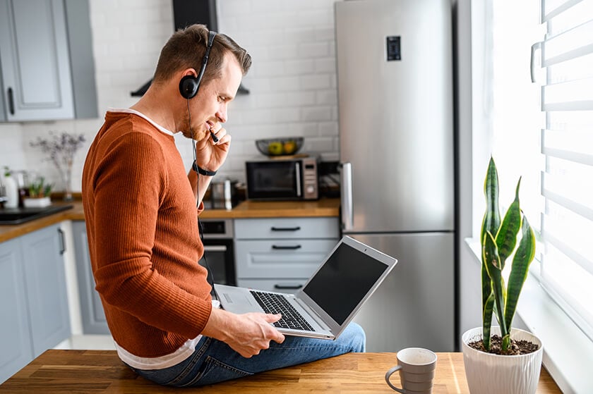 man holding laptop in kitchen with headset remote working
