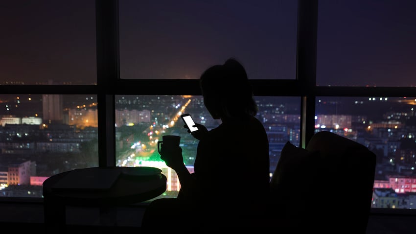 Silhouette of a woman on smartphone overlooking city at night