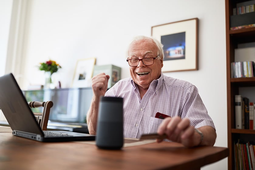 Idoso fazendo compras online com cartão de crédito, laptop e dispositivo de caixa de som inteligente.